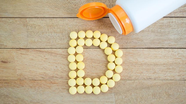Yellow pills forming shape to D alphabet on wood background